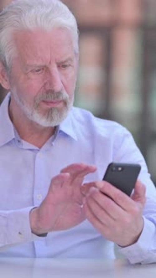 Senior Man Using Smartphone at Table Indoors