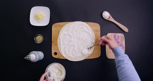 birdeye shot of making a vegan tarte flambée oder vegetarische pizza with spices, oil and vegan che