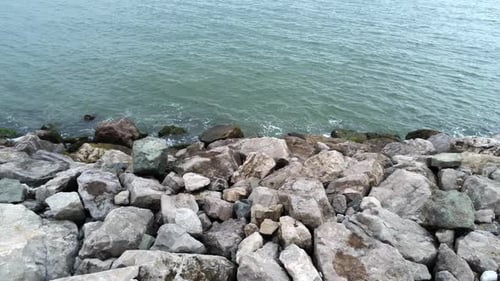 Aerial view above splashing ocean tide breaking on rocky coastal shoreline slow left dolly