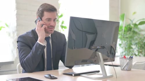 Man in Suit Answering Cellphone at Desk