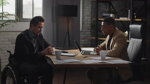 Two Men in Business Suits are Sitting at a Table in an Office and Discussing Something A Man in a