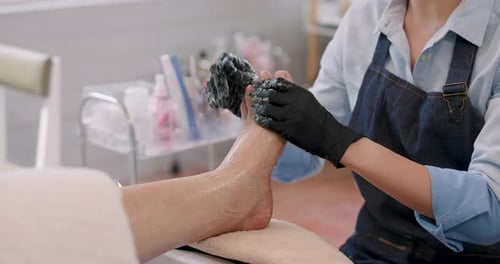 Asian spa owner massaging elderly female client’s foot during pedicure treatment, applying
