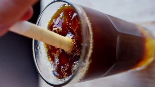 Cold brew coffee and bubble tea in a glass with ice and big white straw close up slow motion, vertic