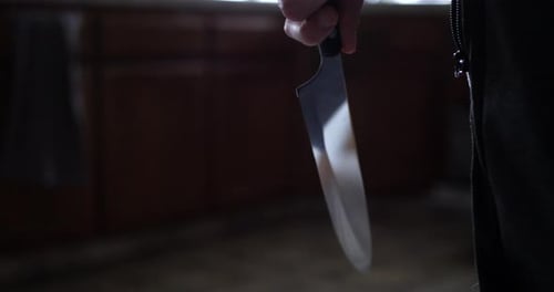 A scary slasher killer holding a kitchen knife and walking towards his murder victim in their home.