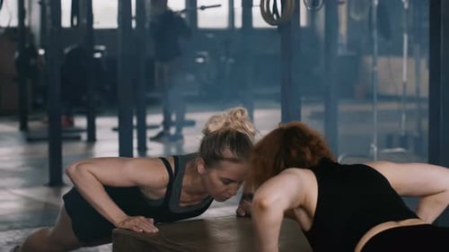 Glückliche attraktive junge blonde Frau trainiert mit einer Fitnesstrainerin im Fitnessstudio und macht Liegestütze