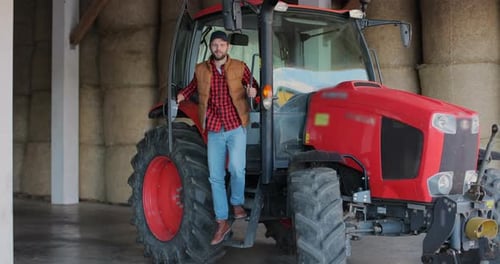Young Adult Farmer Poses with Tractor in Barn