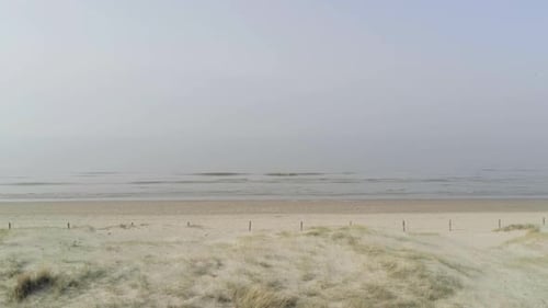 Calm waves wash upon a calm beach, distant horizon fades into the haze, aerial track