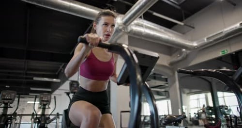 A Young Beautiful Woman in Sportswear is Training and Exercising on an Exercise Bike in a Gym