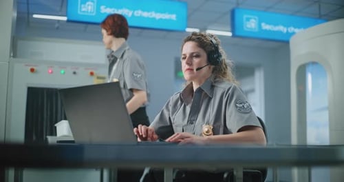 Airport Security Checkpoint Female Security Officer in Headset Using Laptop Looking at Camera
