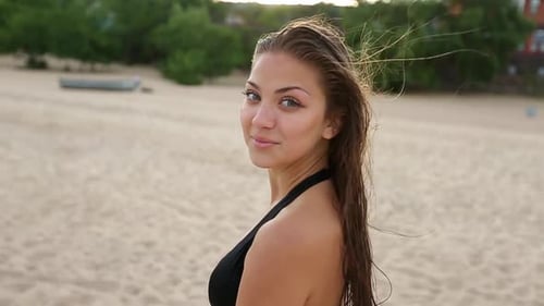Joven juguetona y risueña caminando junto al mar en una playa tropical durante la puesta de sol y mira hacia atrás