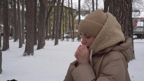 A Girl on the Street Warms Her Hands By Breathing on Them In the Winter Park