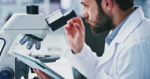 Focused Scientist Using Microscope and Tablet in Lab