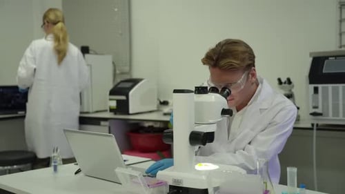 Scientist Using Microscope and Typing on Laptop