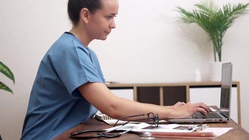 Woman in Scrubs Typing on Laptop at Desk