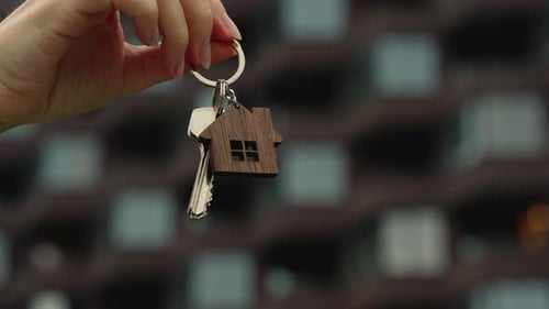 Hand Holding a Key Against the Background of an Apartment Building The Concept of a New Home