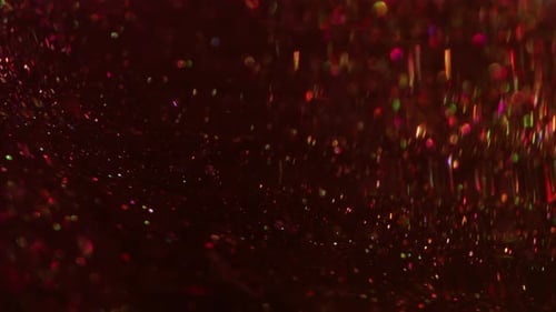 Shimmering Multicolored Glitter Particles Floating on Dark Red Surface