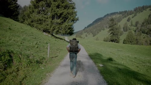 Gimbal tracking backpacker in casual clothing hiking on rural dirt road in mountain valley
