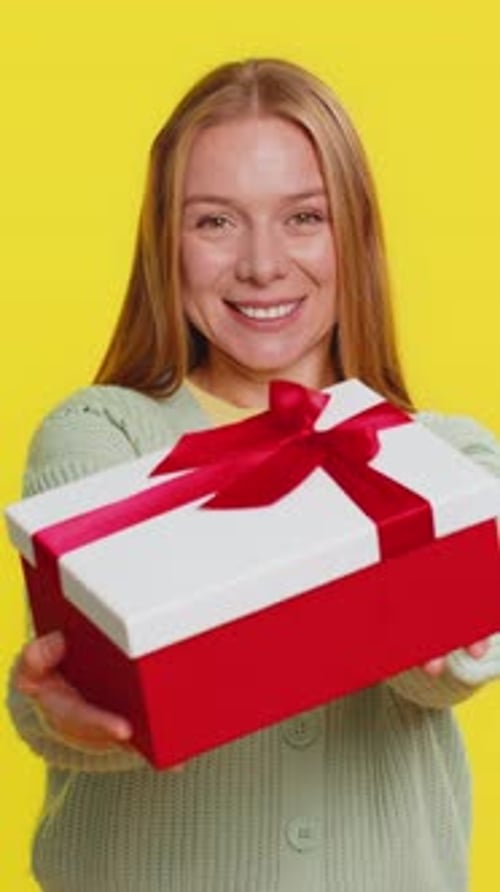 Smiling Woman Presents Gift on Yellow Background