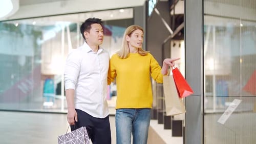 happy multiracial couple asian man and caucasian woman walking together in mall after shopping