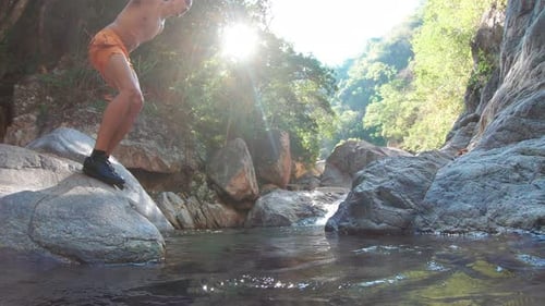 Man is overcoming an obstacle by jumping over the stream slowmo low angle