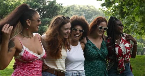 Um grupo de moças multiétnicas caminhando no parque enquanto se abraçam,