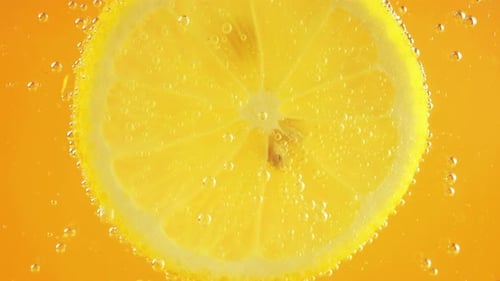 Eine Scheibe reifer Zitrone im Wasser sprudelt auf einem orangefarbenen Hintergrund.