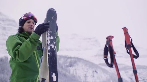 Male Skier Putting Skins on Skis Below Snowy Winter Mountain Active