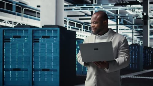 Smiling Engineer in Data Center Managing Software Using Laptop