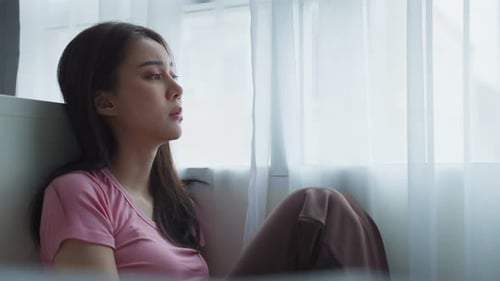 Asian young upset depressed woman sitting alone in living room at home.