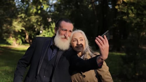 An Elderly Couple Happily Taking a Selfie in a Beautiful Park with Nature and Sunshine