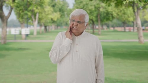 Sick Indian old man suffering from tooth pain in park