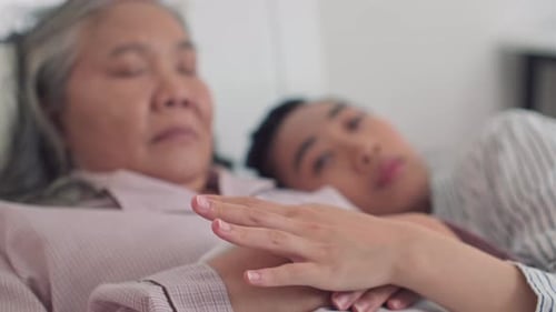 Triste hija asiática acostada sobre el pecho de su anciana madre enferma