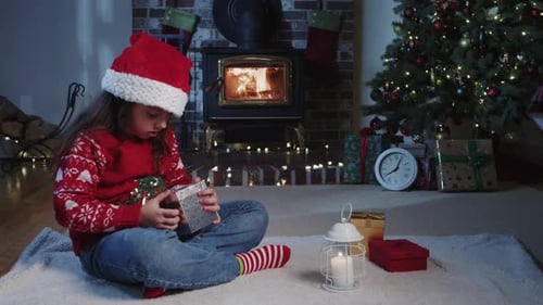Girl Unwrapping Christmas Gift by Fireplace