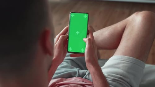 Man Using Smartphone in Vertical Mode with Green Mockup Screen Doing Swiping Scrolling Gestures Guy