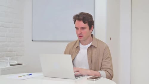 Frustrated Man Working on Laptop in Bright Office