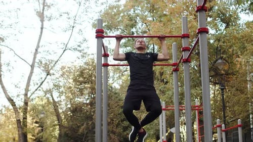 Junger kaukasischer Athlet in Sportbekleidung macht intensiv Klimmzüge in einem Outdoor-Trainingsbereich