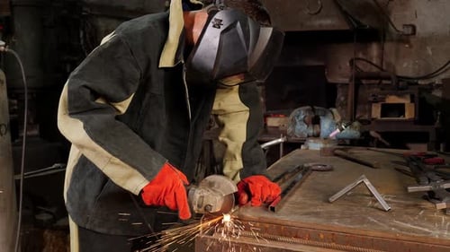 Young Manual Worker Using Grinder on Metal in Factory