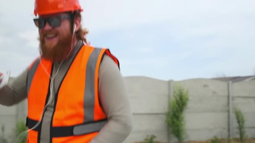 Belo trabalhador da construção civil dançando, ouvindo música, saindo de férias, curtindo uma pausa nos fones de ouvido