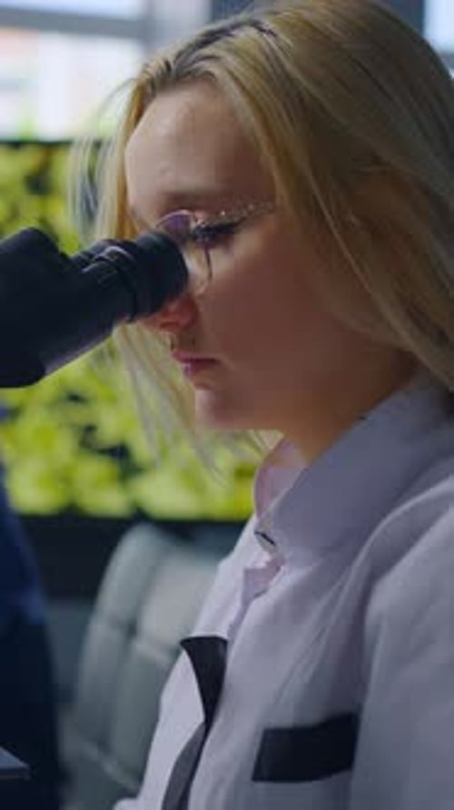 Focused Young Woman Using Microscope in Bright Lab