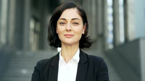 Close up portrait of a young serious businesswoman standing on the street near an office building.