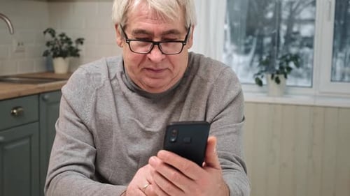 Senior Man Uses Smartphone Indoors in Kitchen