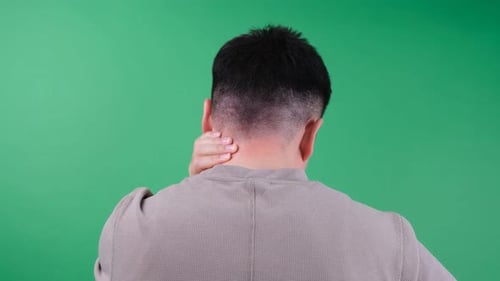 Man rubbing neck on green screen background