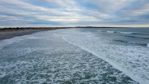 Aerial of ocean waves crashing on a beach on a cloudy day. Drone of sea water on the coast during a