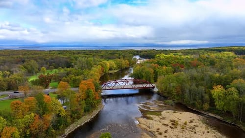 Approaching a little metal bridge crossing the narrow river. Black car crosses the bridge.