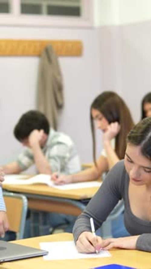Teacher Assists Student Writing in Classroom