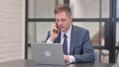 Man in Suit on Phone While Using Laptop