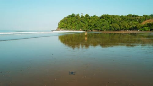Wide aerial view of woman walking on wet sand beach in Costa Rica jungle