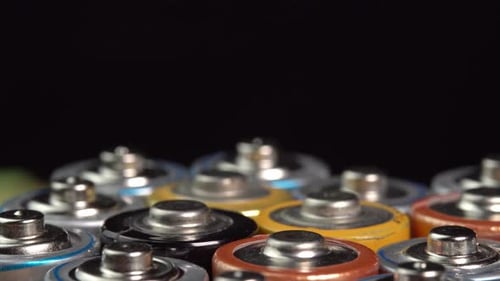Rows of used alkaline AA batteries rotate on black background. Lithium ion battery pack close up