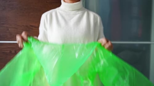 Young Woman Putting on Green Raincoat Over Sweater in Front of Wardrobe at Home Protection From Rain