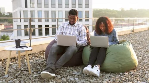 Smiling African Couple Sitting at Beanbags at Rooftop of Office